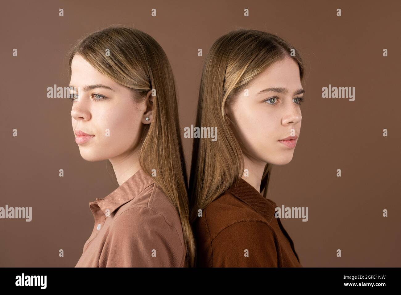 Due ragazze gemelle graziose in camicie che toccano dalle loro spalle mentre si levano in piedi davanti alla macchina fotografica Foto Stock
