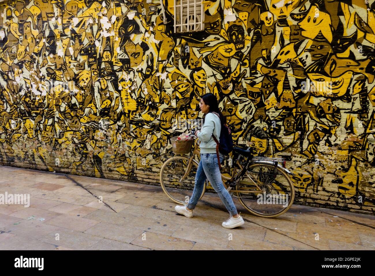 Una donna con una bicicletta cammina lungo il muro della Spagna Valencia Street art quartiere El Carmen donna che spinge in bicicletta Foto Stock