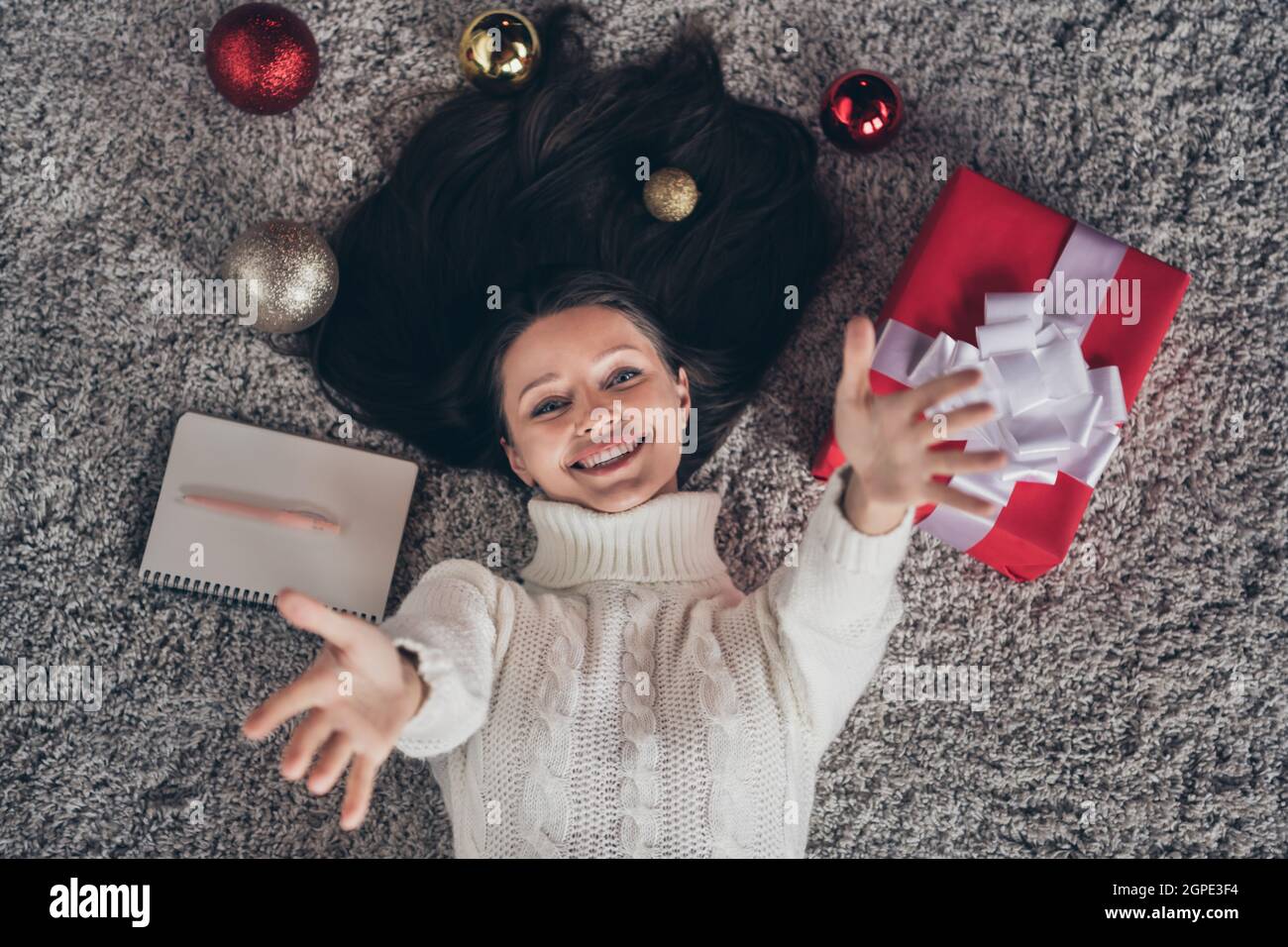 Foto di bella sognante giovane donna vestita maglione lavorato a maglia che giace pavimento sollevando braccia sorridenti casa stanza interna Foto Stock