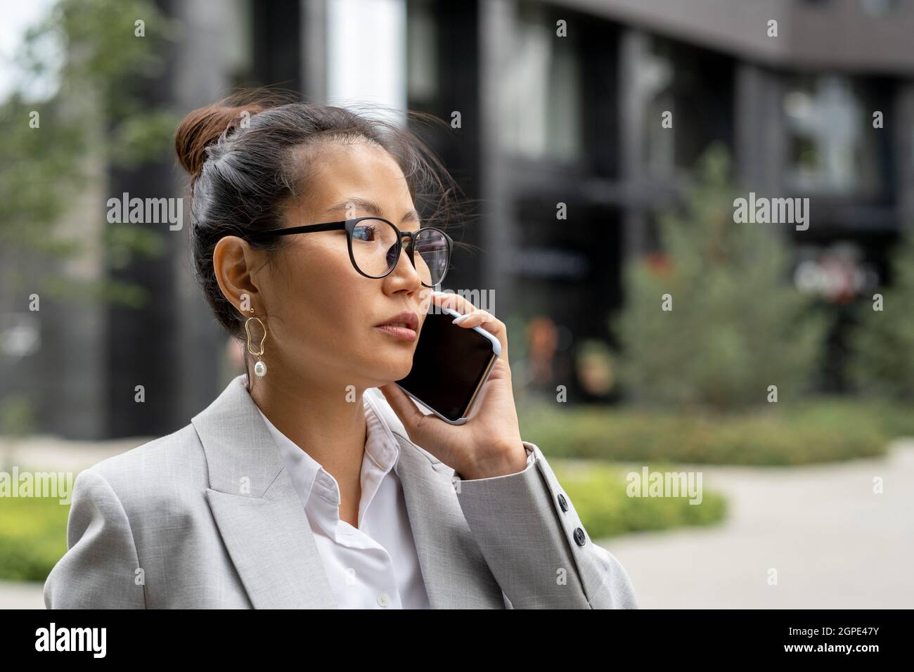 Giovane donna d'affari asiatica seria con smartphone da EAR che chiama partner d'affari Foto Stock