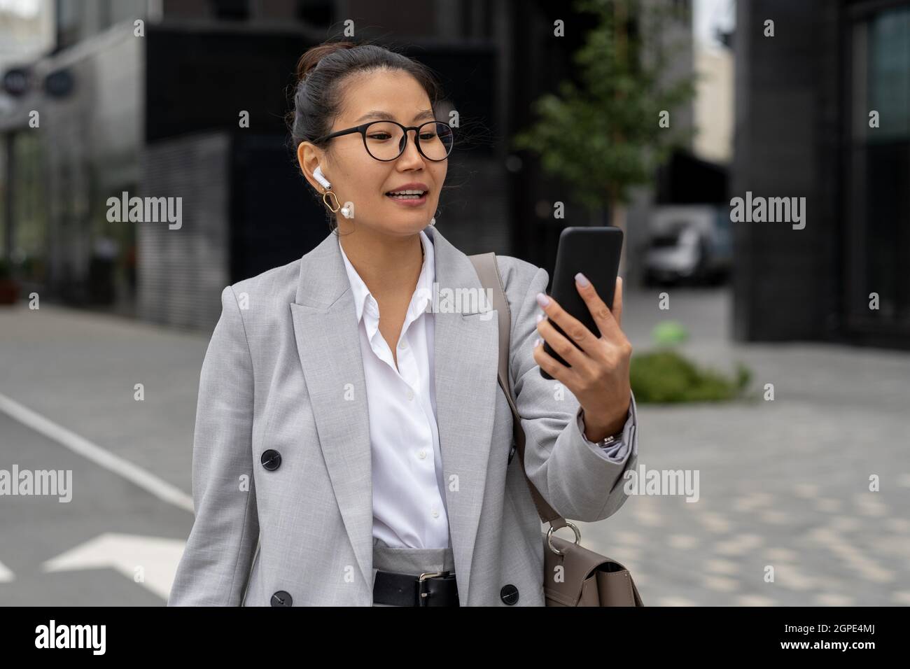 Felice giovane donna d'affari makig videochiamata mentre si cammina da solo edifici contemporanei Foto Stock