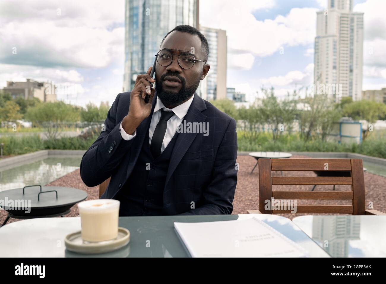 Giovane uomo d'affari africano che parla con lo smartphone mentre beve un drink in un bar all'aperto Foto Stock