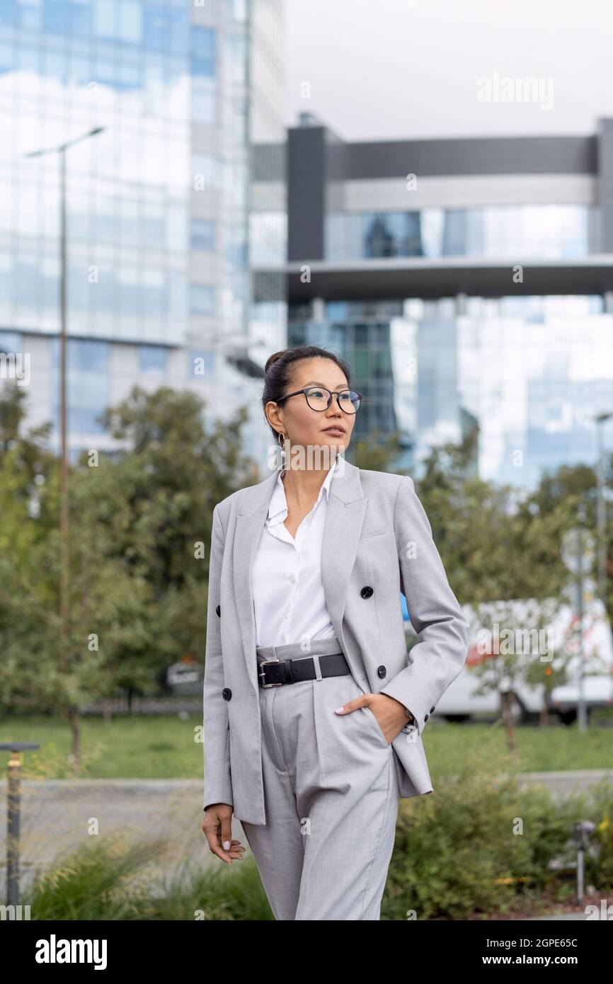 Giovane ed elegante donna asiatica in abito grigio contro l'ambiente urbano Foto Stock