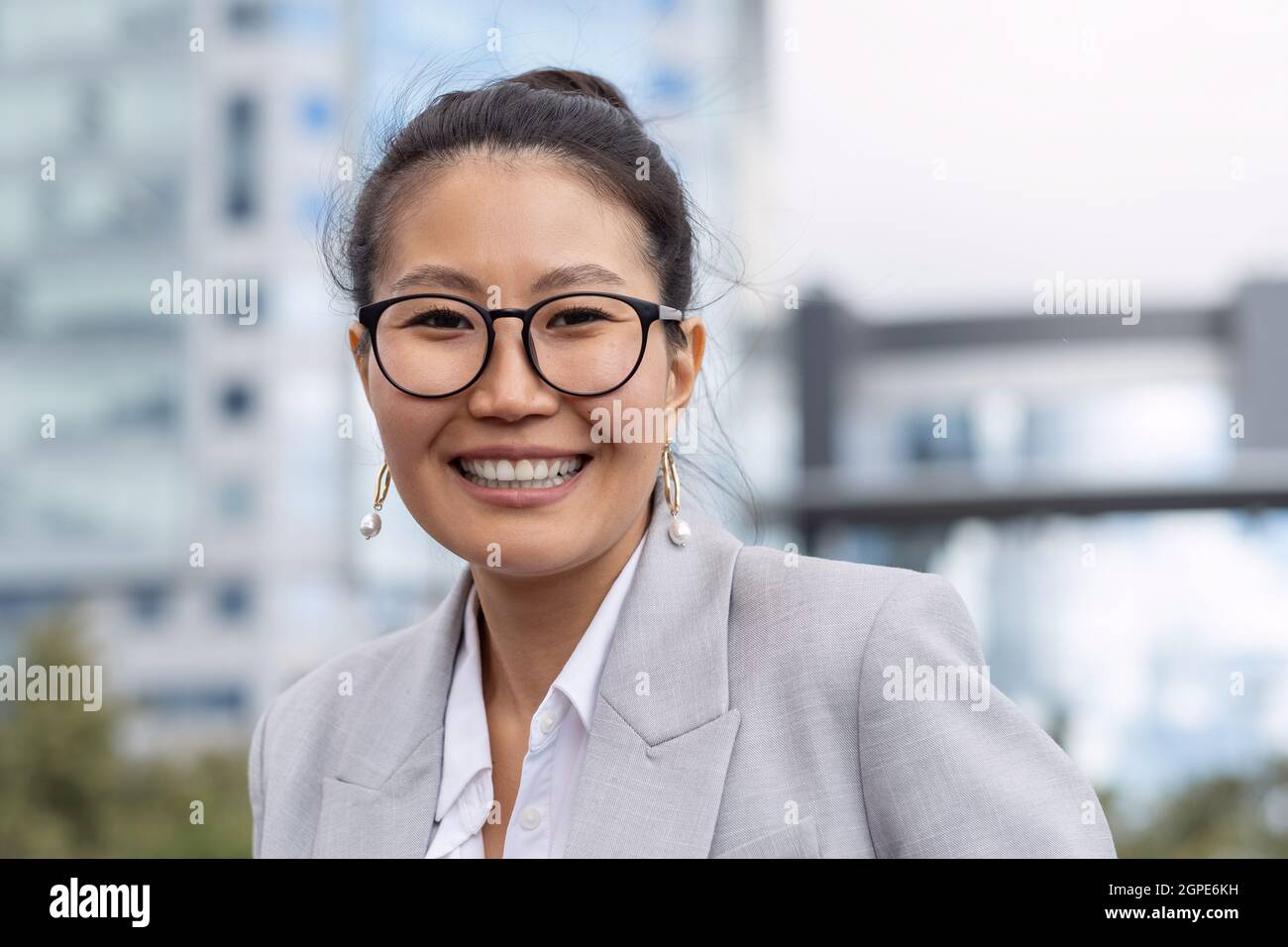 Giovane donna d'affari allegra in occhiali e vestito grigio che ti guarda con un sorriso toothy Foto Stock