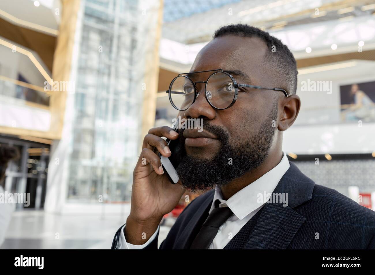 Uomo d'affari contemporaneo con smartphone telefonando all'orecchio nel business center Foto Stock