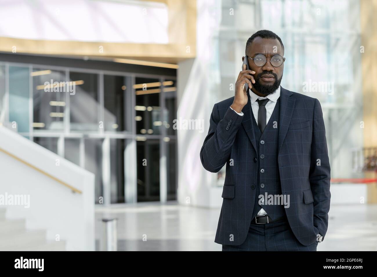 Giovane imprenditore africano che parla con un collega su smartphone in un grande centro commerciale Foto Stock