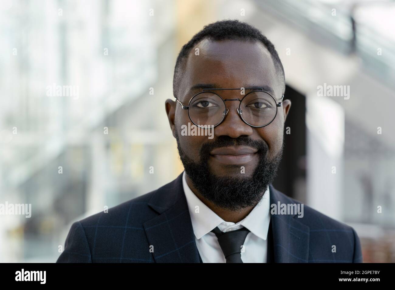 Giovane uomo sorridente in occhiali e abito elegante che ti guarda in centro commerciale Foto Stock