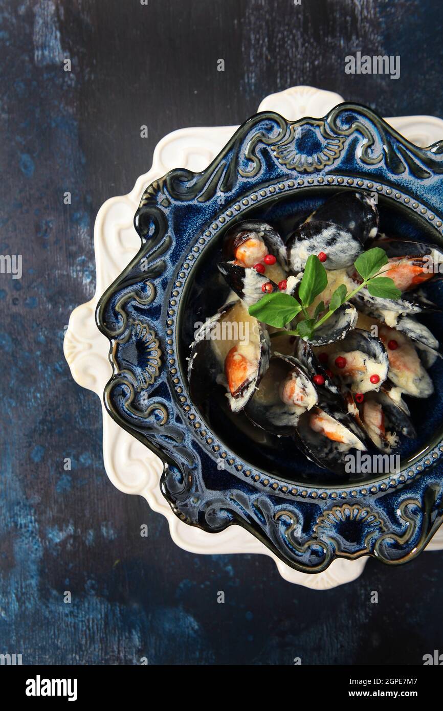 Cozze in salsa di panna. Frutti di mare su un piatto. Elegante vasellame in ceramica blu. Vista dall'alto. Sfondo blu con texture. Foto verticale. Primo piano. Foto Stock