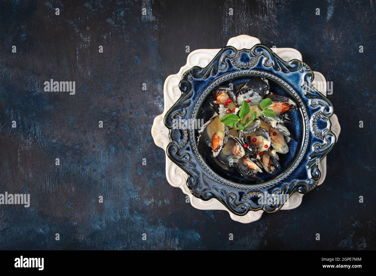 Cozze in salsa di panna. Frutti di mare su un piatto. Elegante vasellame in ceramica blu. Vista dall'alto. Sfondo blu. Spazio libero. Foto Stock