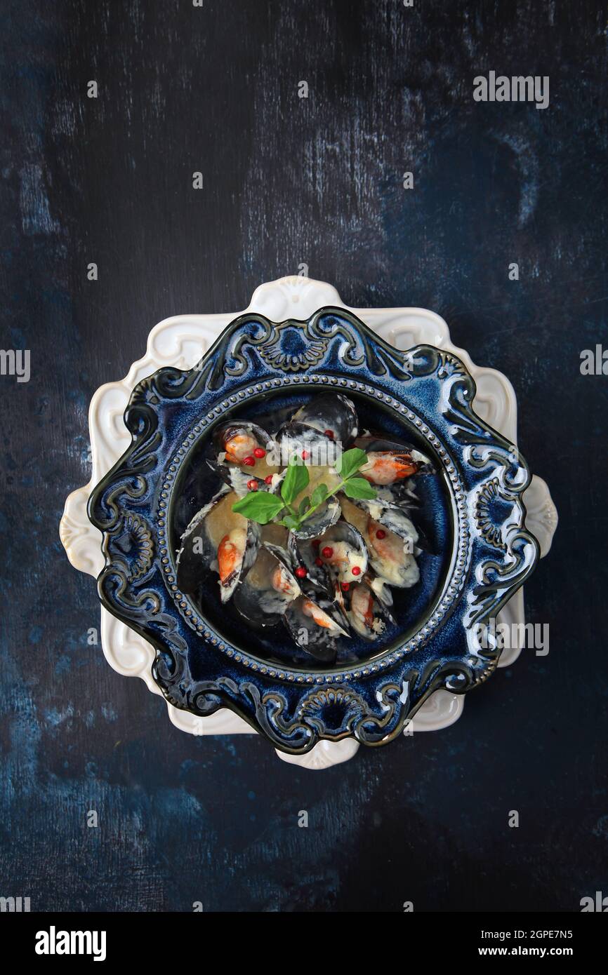Cozze in salsa di panna. Frutti di mare su un piatto. Elegante vasellame in ceramica blu. Vista dall'alto. Sfondo blu. Spazio libero. Foto verticale. Foto Stock