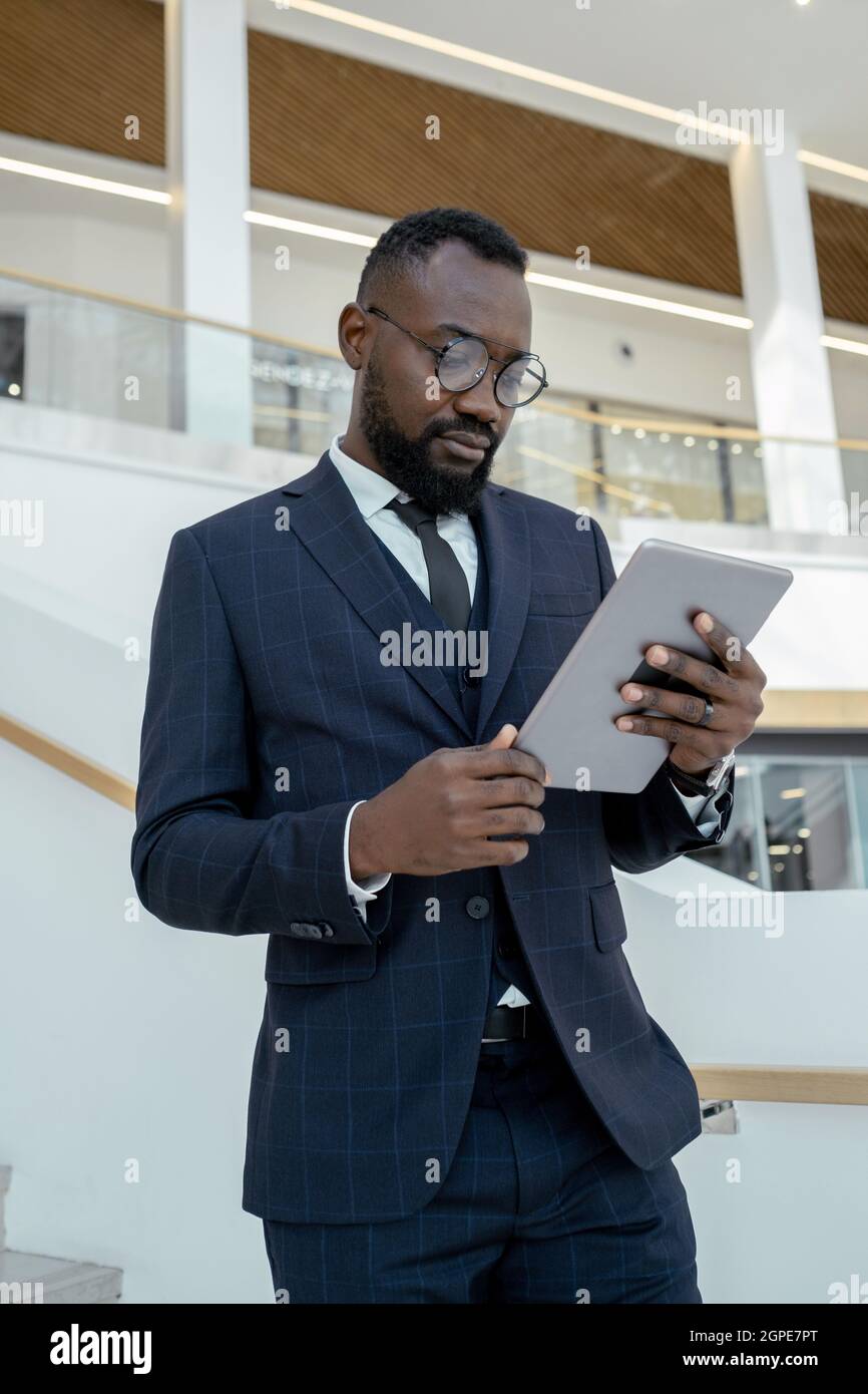 Giovane uomo serio in abito elegante guardando lo schermo del tablet mentre legge le notizie online Foto Stock