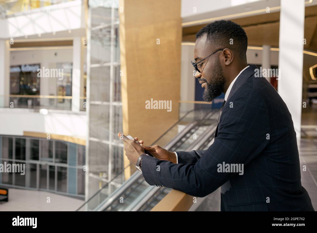 Vista laterale dell'elegante uomo d'affari che guarda allo schermo dello smartphone all'interno del moderno business center Foto Stock