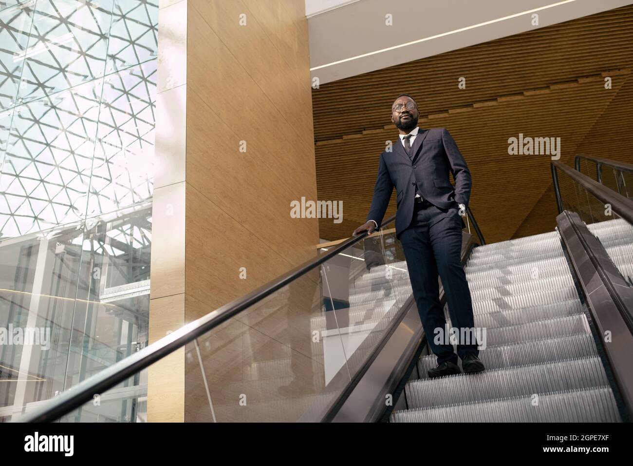 Uomo d'affari africano in abito elegante in piedi sul passo di mobile scala mobile nel centro commerciale Foto Stock