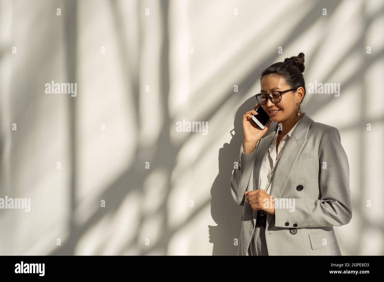 Felice giovane donna d'affari asiatica che parla al telefono cellulare contro il muro bianco Foto Stock