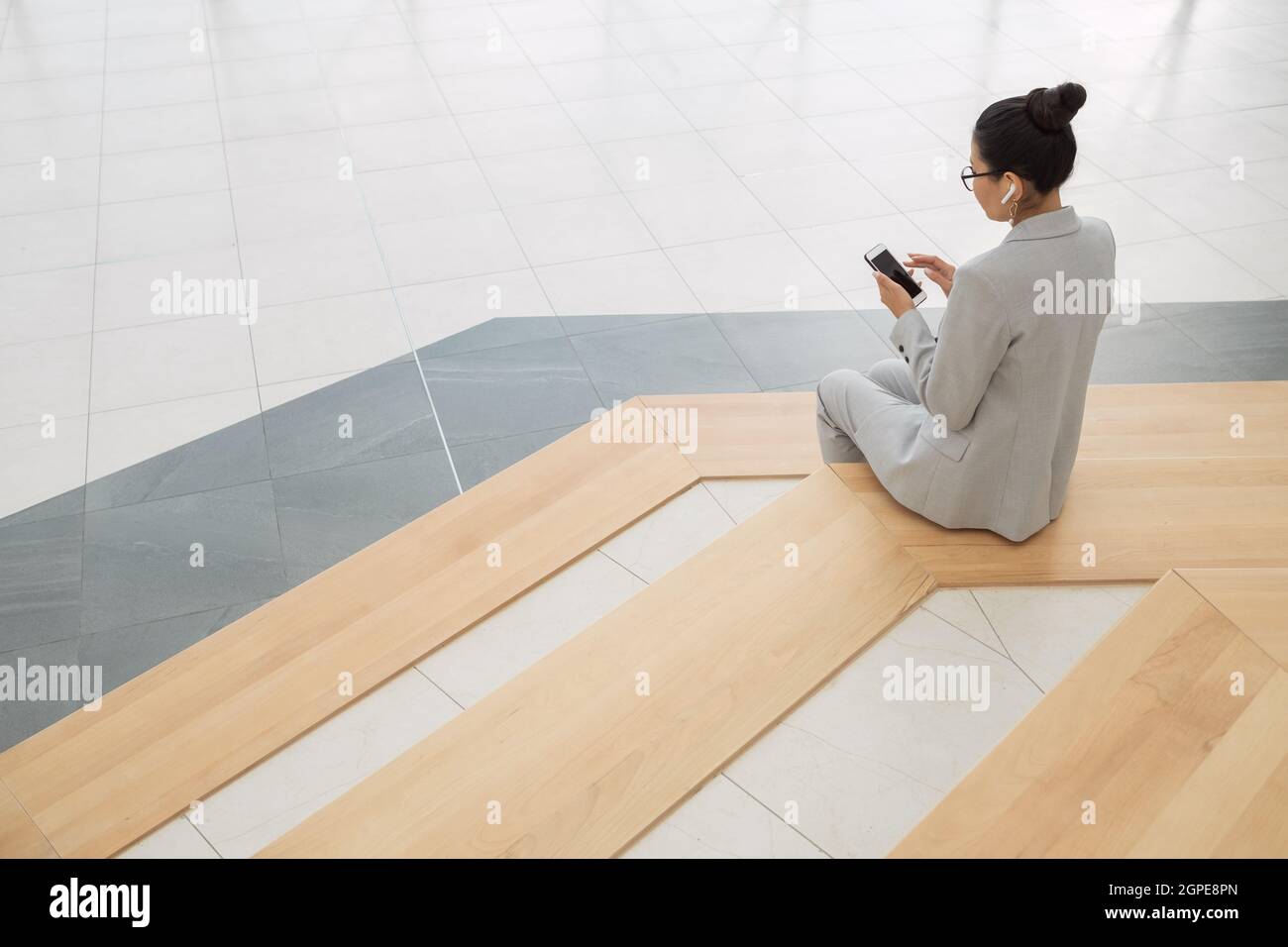 Giovane donna d'affari riposante in abito grigio che ascolta musica mentre si siede su grandi passi Foto Stock