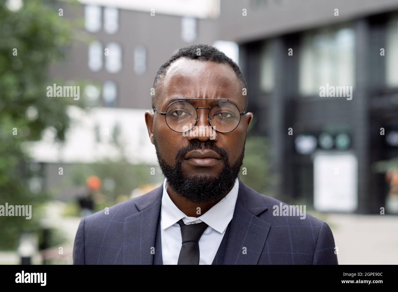 Giovane uomo d'affari serio in occhiali e vestito in piedi contro l'architettura moderna Foto Stock
