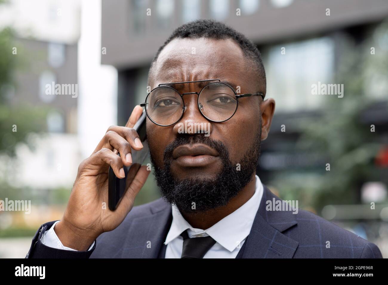 Faccia di giovane uomo d'affari elegante in occhiali che parlano sul telefono cellulare all'aperto Foto Stock