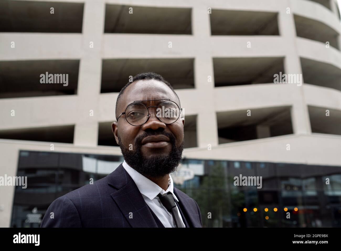 Giovane banchiere africano in occhiali e formalwear in piedi in ambiente urbano Foto Stock