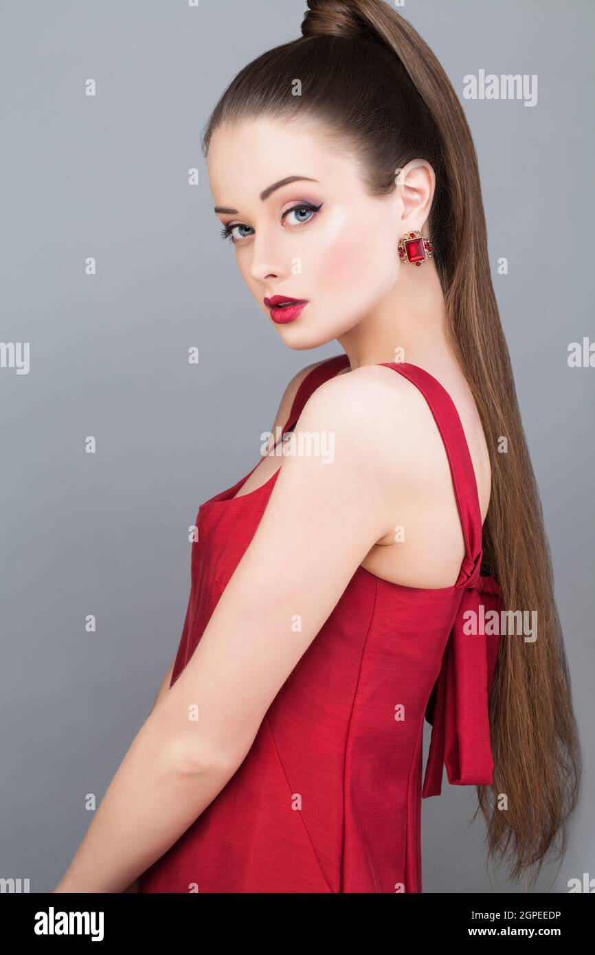 Bella modella moda donna glamour con coda di pony hairstyle vestito rosso e orecchino dorato Foto Stock