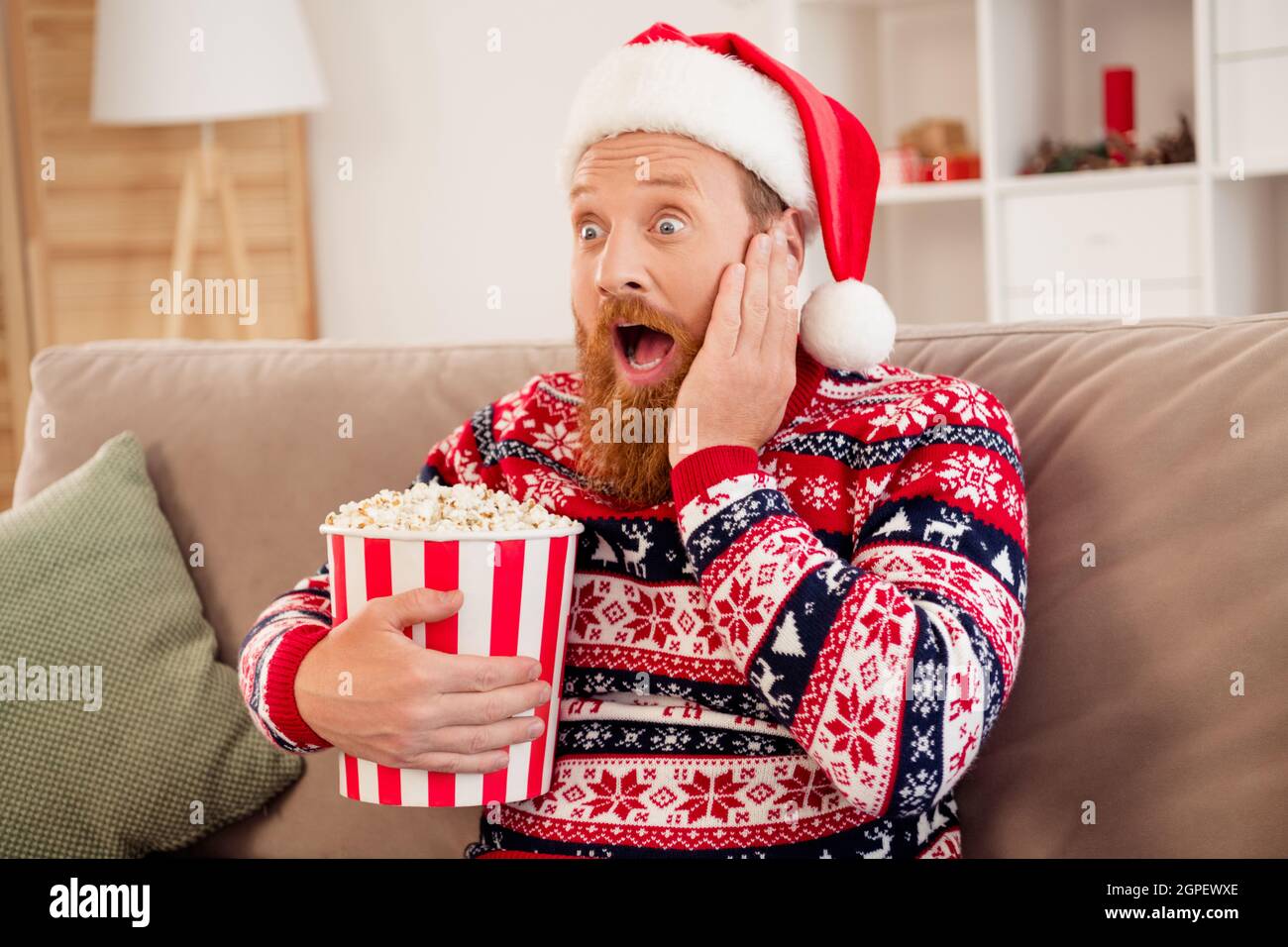 Foto di giovane uomo stupito scioccato sorpreso omg wow reazione tenere popcorn box guardare film thriller nuovo anno in casa Foto Stock