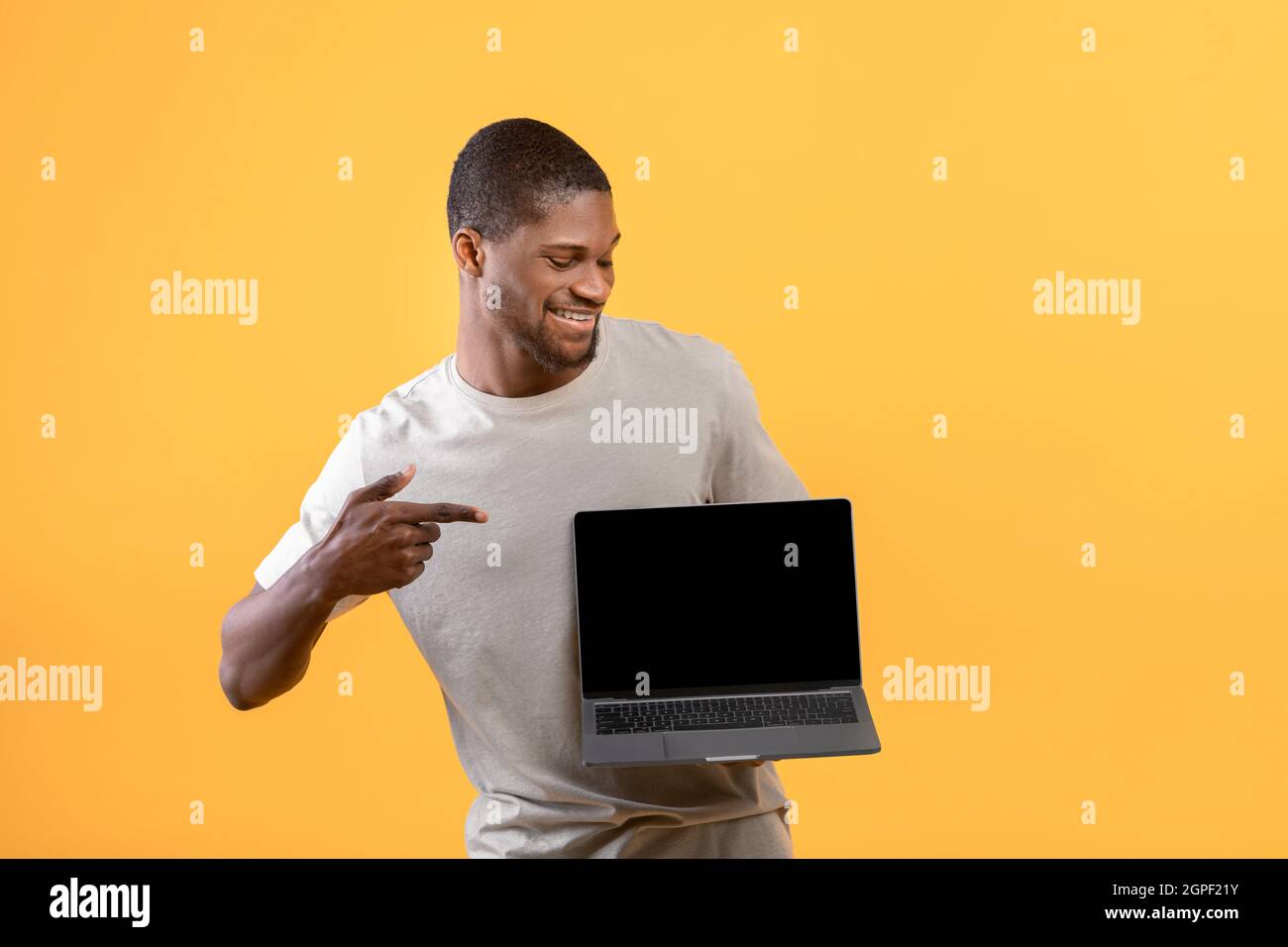Felice afroamericano che punta allo schermo vuoto del laptop, mockup per il vostro Web site o disegno dell'annuncio sopra lo sfondo giallo Foto Stock