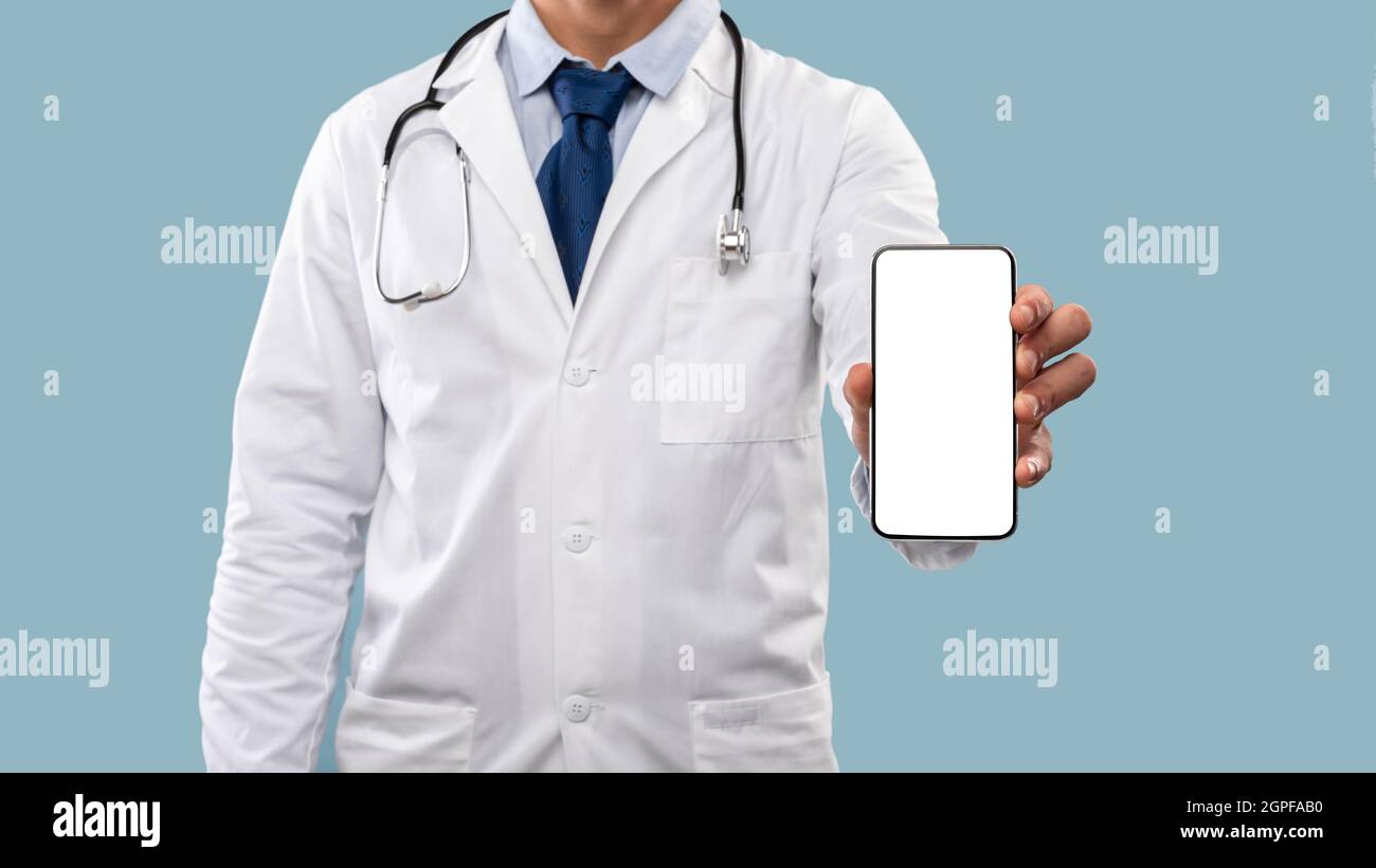 Medico maschio irriconoscibile che mostra lo schermo del telefono cellulare su sfondo blu Foto Stock