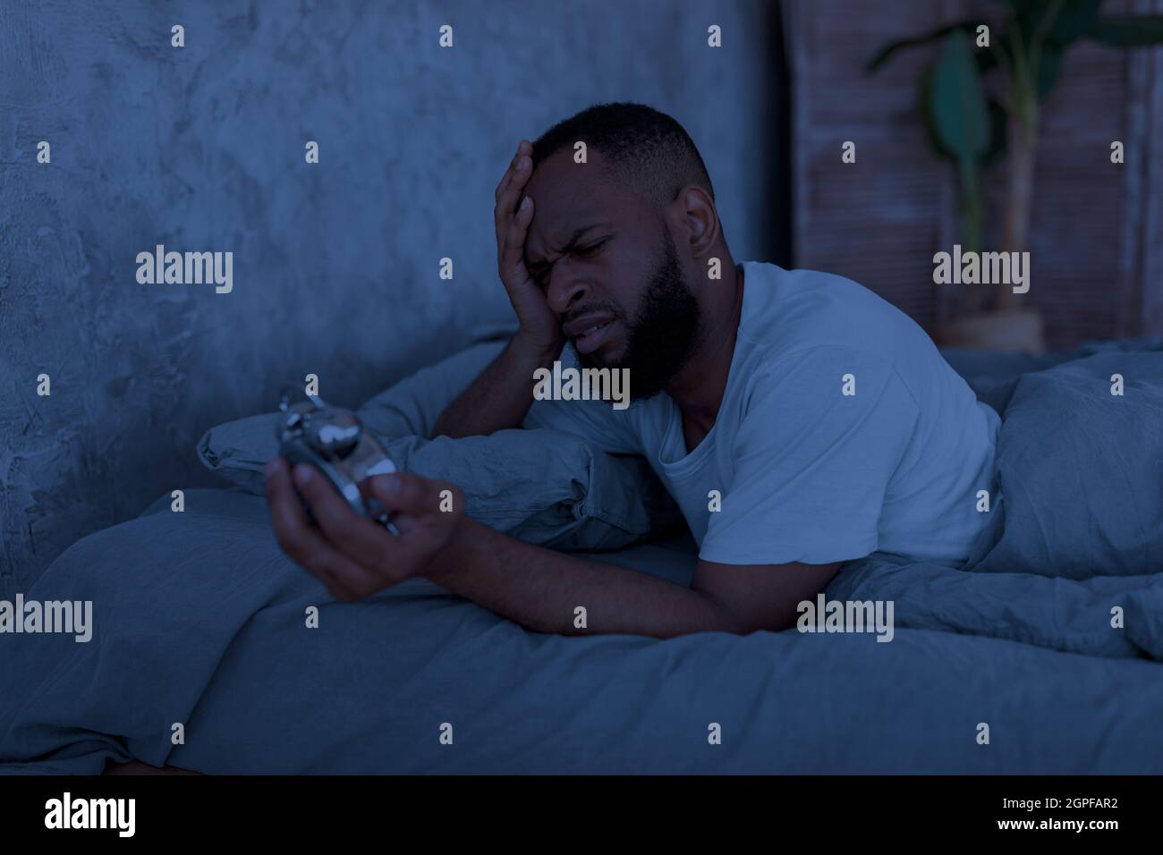 Uomo nero che soffre di insonnia guardando l'orologio Foto Stock