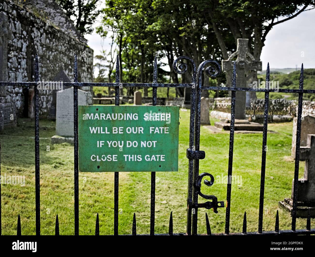 Divertente cartello all'ingresso del cortile della chiesa di Kildalton con Kildalton Cross sullo sfondo Foto Stock