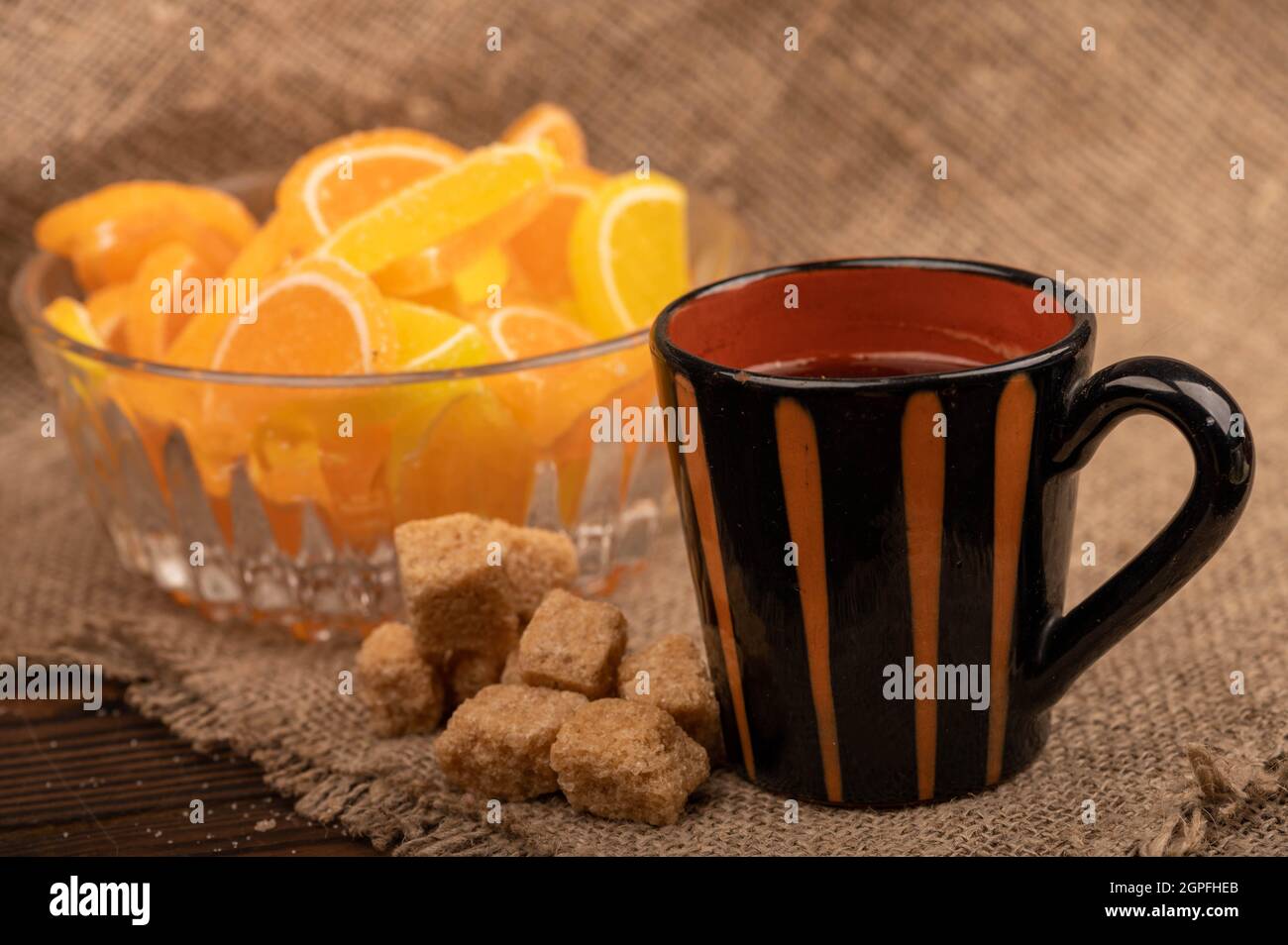 Fette di limone di marmellata multicolore in vaso di vetro, pezzi di zucchero di canna e una tazza di caffè, primo piano, fuoco selettivo Foto Stock