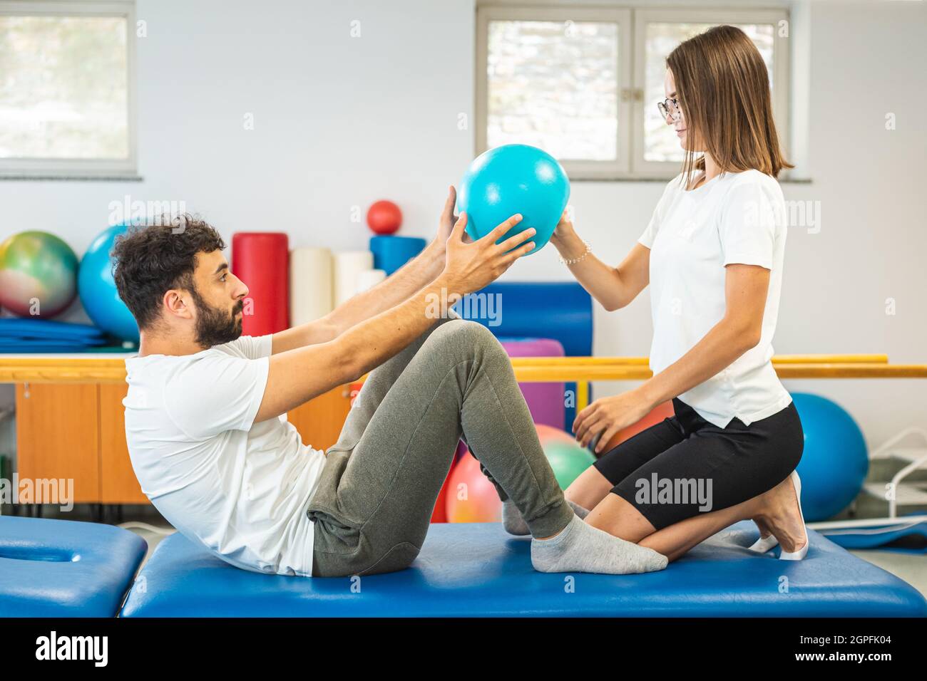 Fisioterapista femminile e paziente maschile durante la terapia di riabilitazione. Esercizi di rafforzamento Ccore con pallina pilates con assistenza terapista. Foto Stock