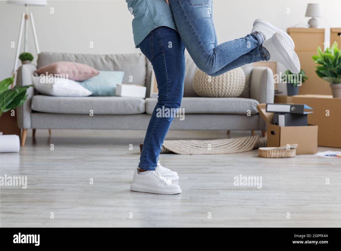 Il giovane marito felice abbraccia e solleva la moglie in un appartamento con scatole di cartone Foto Stock