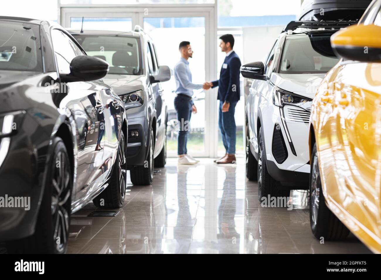 Il cliente e l'assistente alle vendite scuotono le mani e gli interni dello showroom dell'auto Foto Stock