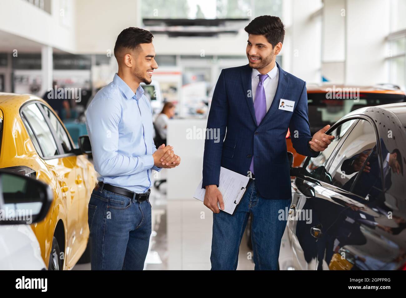 Ragazzo medio-orientale che sceglie la nuova auto, avendo conversazione con il responsabile delle vendite Foto Stock