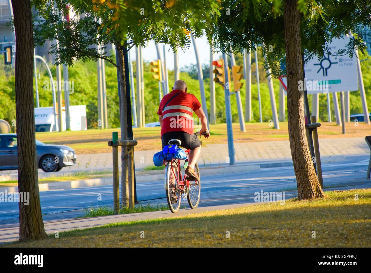 Vista posteriore di un vecchio uomo che guida una bicicletta in una strada. Foto Stock