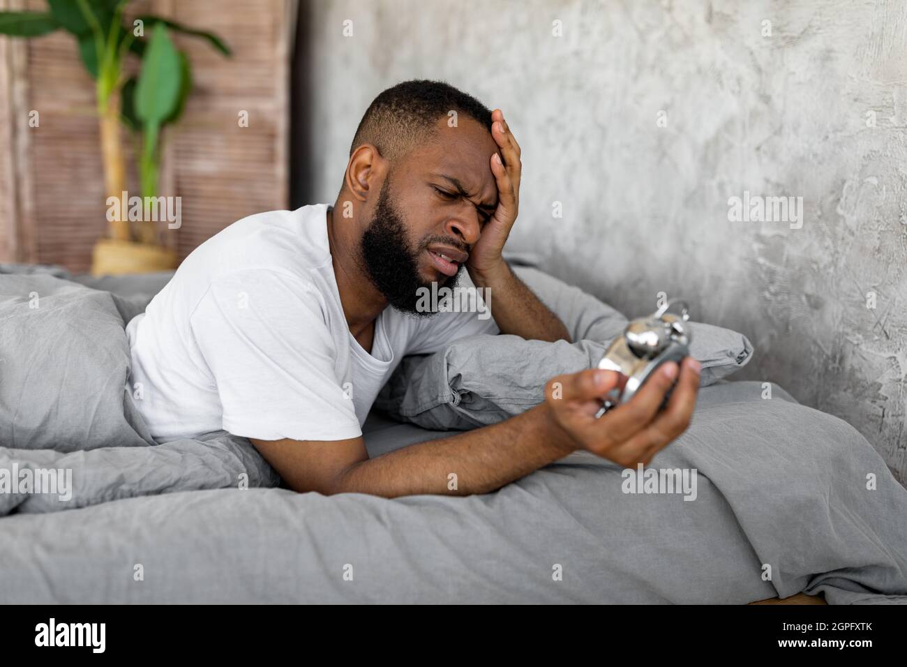 Uomo nero che soffre di insonnia guardando l'orologio a letto Foto Stock