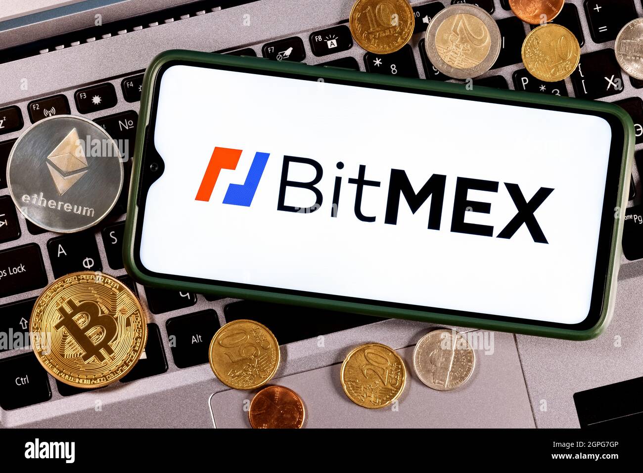 Uno smartphone con il logo BitMEX circondato da monete diverse sullo sfondo del portatile. Foto Stock