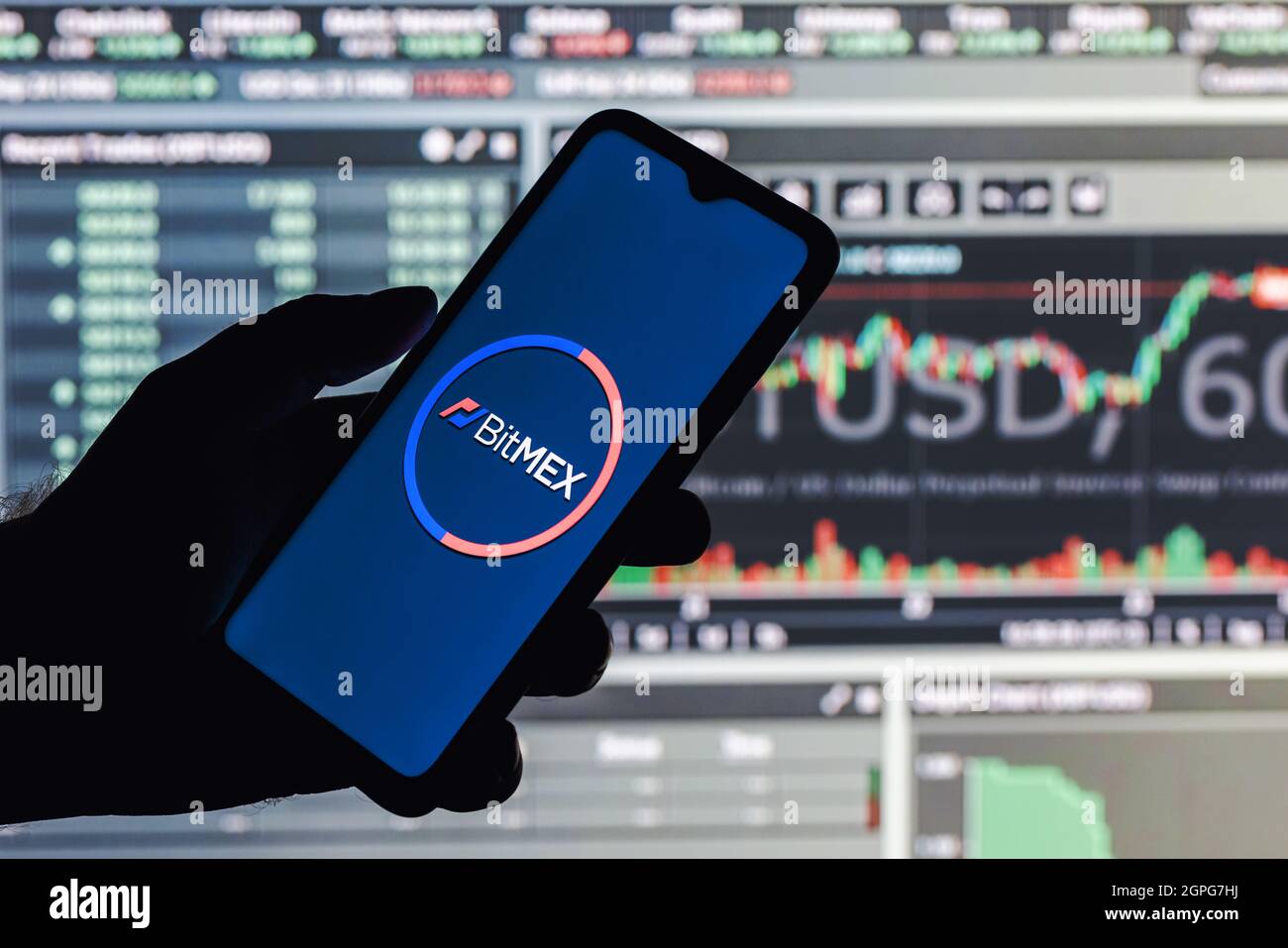 Uno smartphone con il logo BitMEX in mano sullo sfondo della pagina Web di live trading. Foto Stock