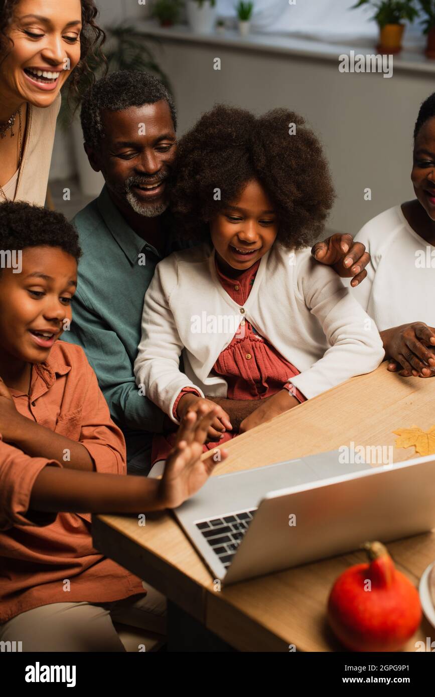 ragazzo afroamericano che agitava la mano vicino al portatile e sorride la famiglia durante la videochiamata il giorno del ringraziamento Foto Stock