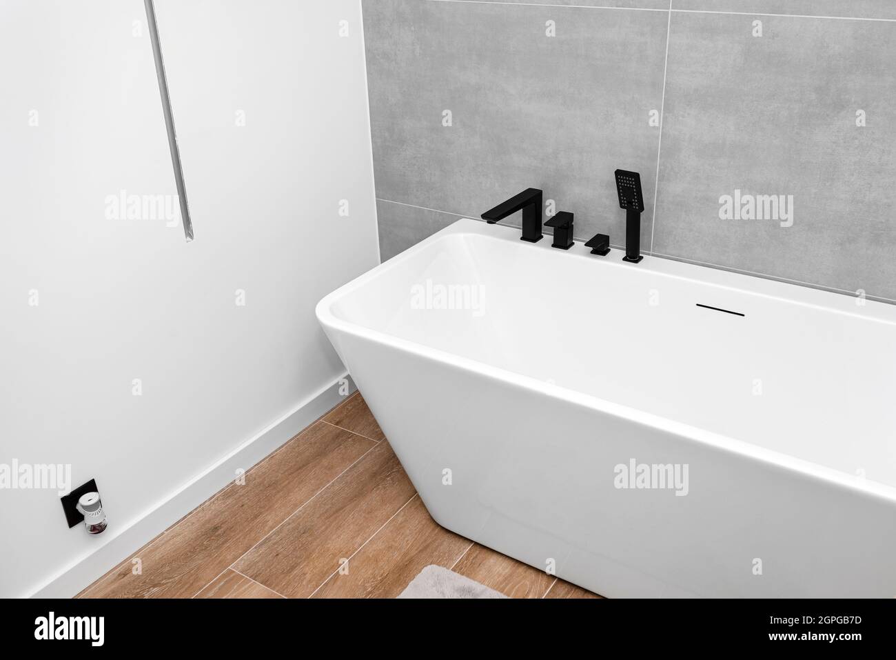 Una moderna vasca da bagno a parete con rubinetto nero opaco, in un bagno rivestito di piastrelle in ceramica. Foto Stock