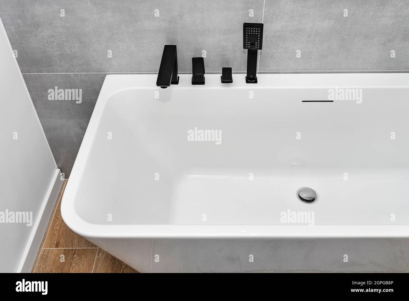 Una moderna vasca da bagno a parete con rubinetto nero opaco, in un bagno rivestito di piastrelle in ceramica. Foto Stock