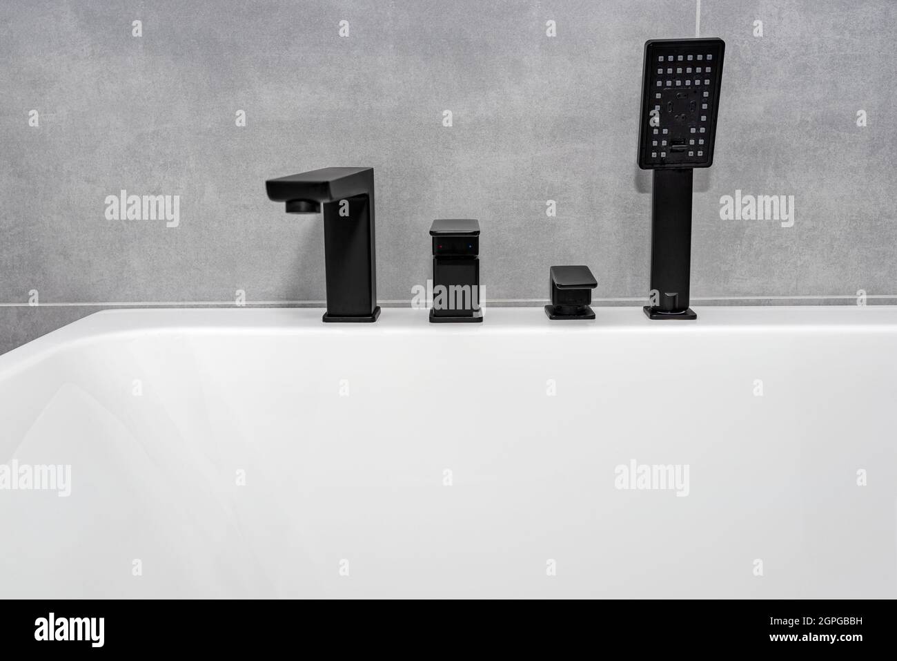 Una moderna vasca da bagno a parete con rubinetto nero opaco, in un bagno rivestito di piastrelle in ceramica. Foto Stock