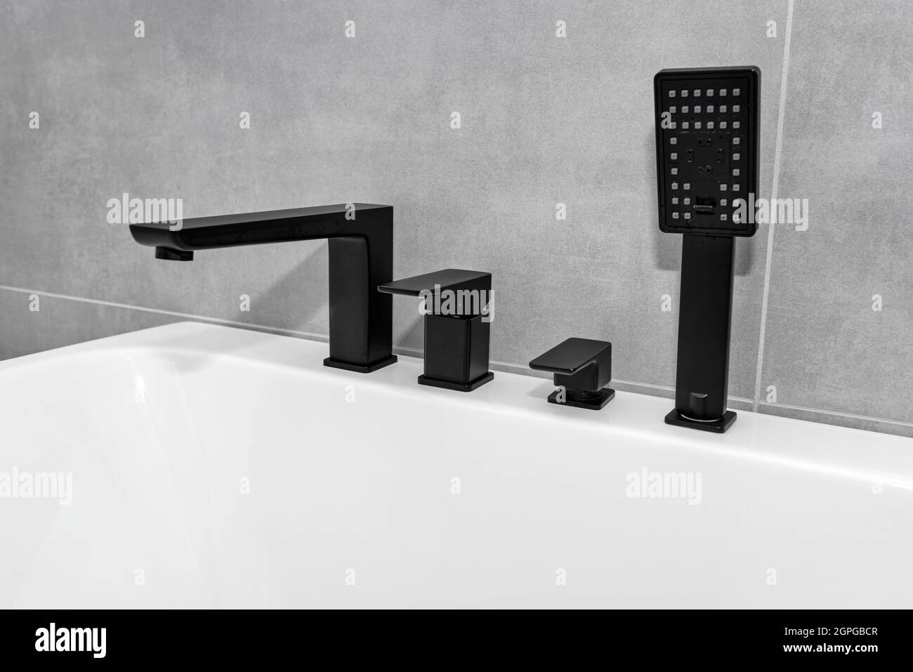 Una moderna vasca da bagno a parete con rubinetto nero opaco, in un bagno rivestito di piastrelle in ceramica. Foto Stock