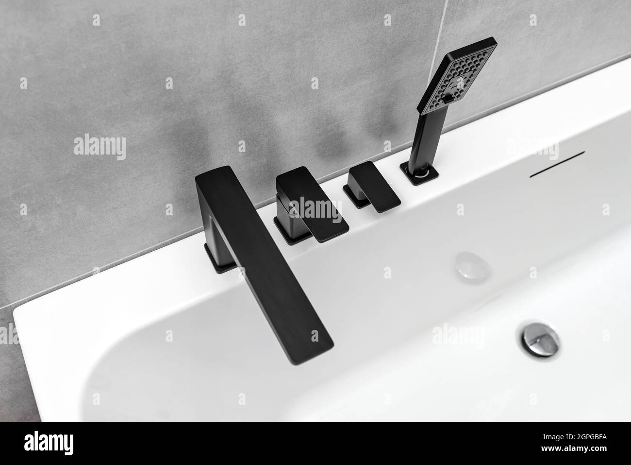 Una moderna vasca da bagno a parete con rubinetto nero opaco, in un bagno rivestito di piastrelle in ceramica. Foto Stock