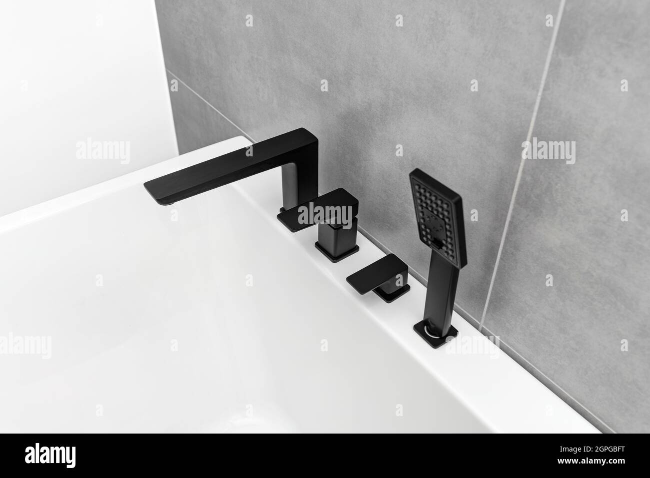 Una moderna vasca da bagno a parete con rubinetto nero opaco, in un bagno rivestito di piastrelle in ceramica. Foto Stock