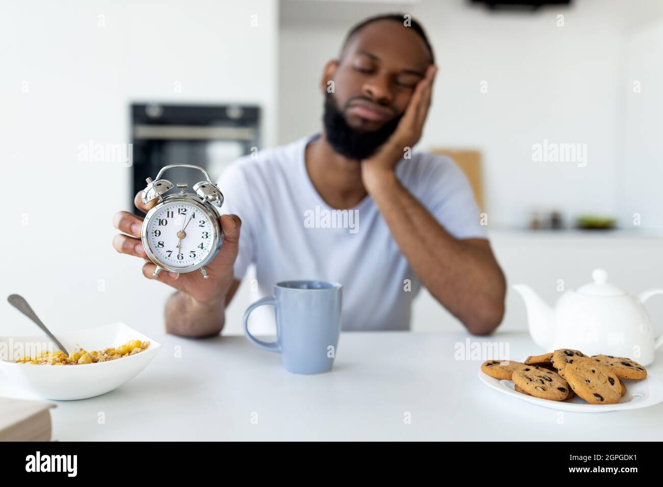 Uomo nero che soffre di insonnia che tiene mostrando sveglia Foto Stock