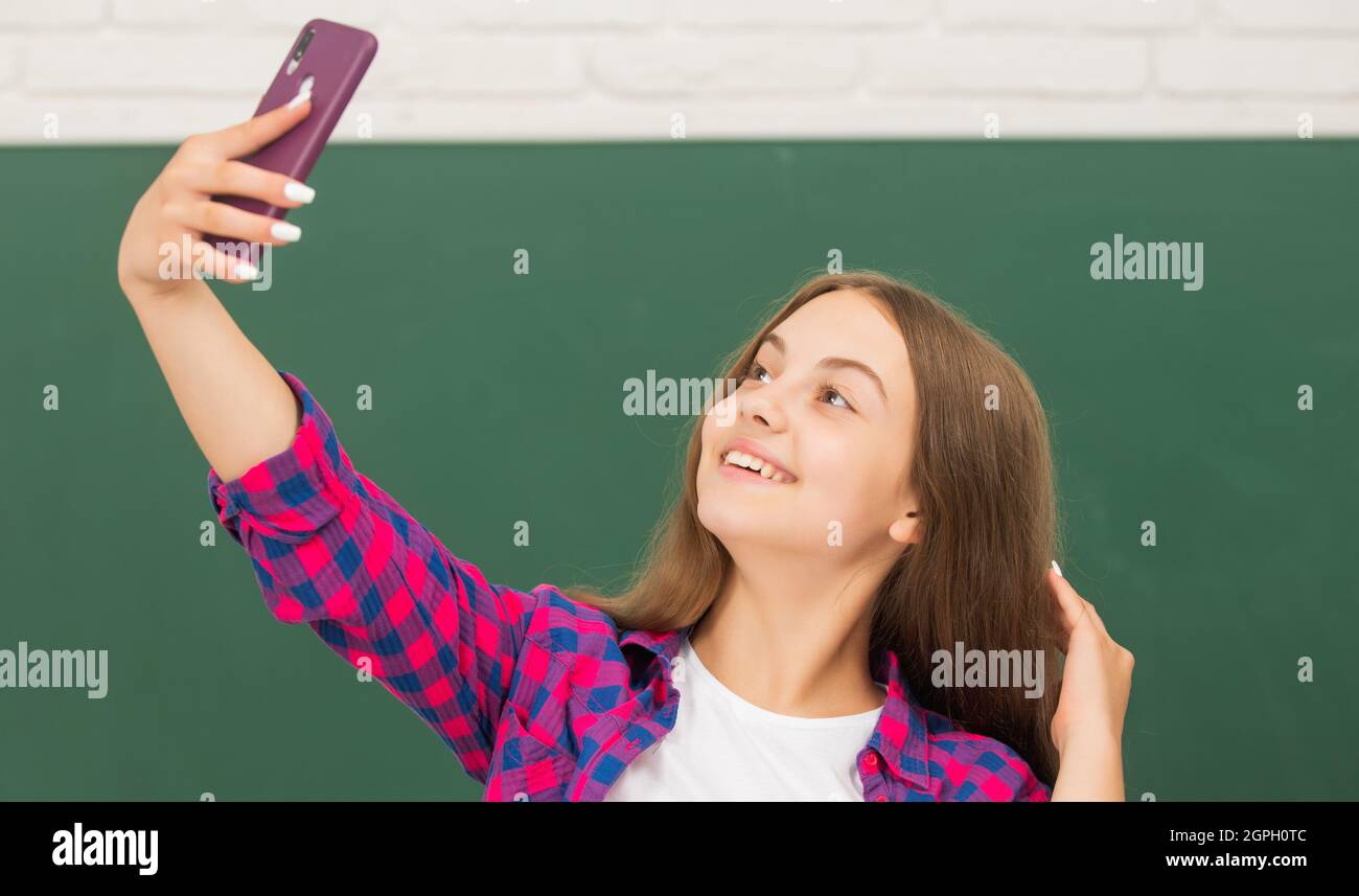 ragazza teen felice facendo selfie sul telefono cellulare in high school a lavagna, selfie Foto Stock