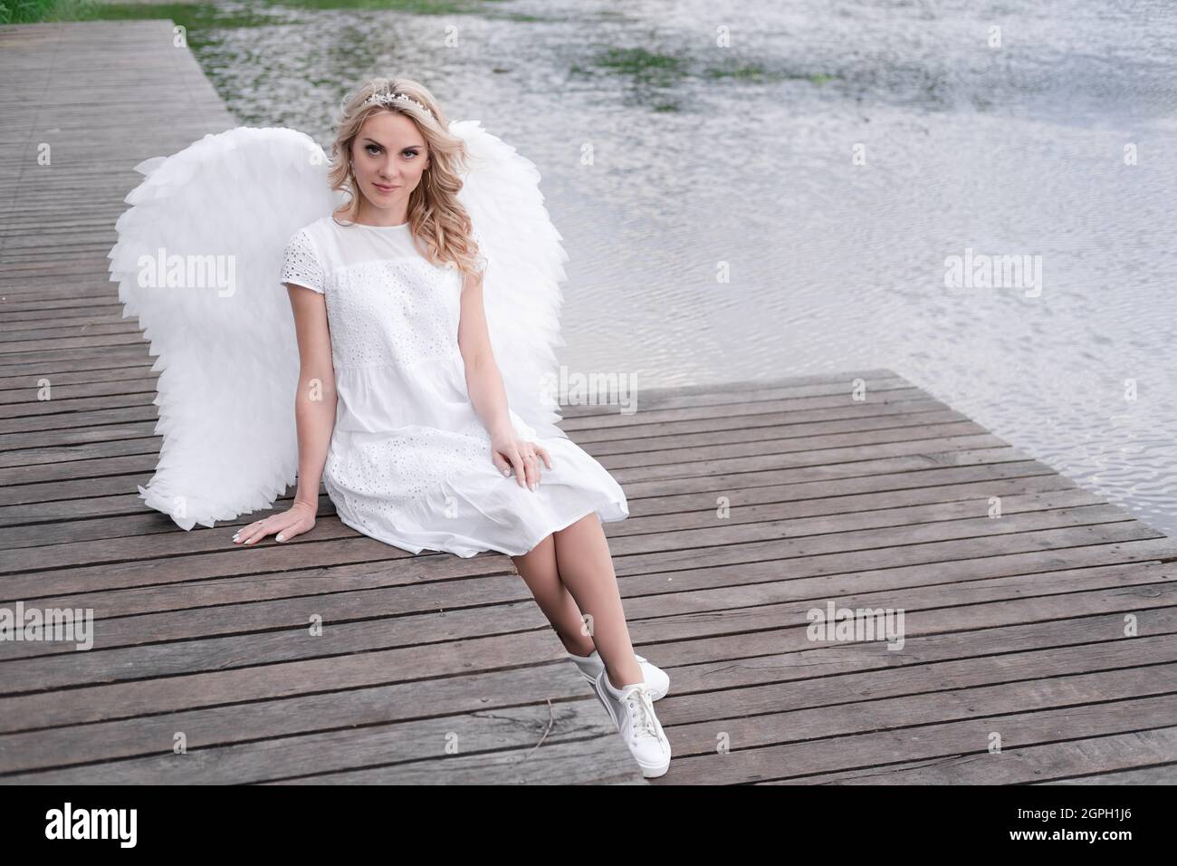 bionda affascinante con ali bianche d'angelo in piedi accanto all'acqua.  bella donna in costume d'angelo. dea Foto stock - Alamy