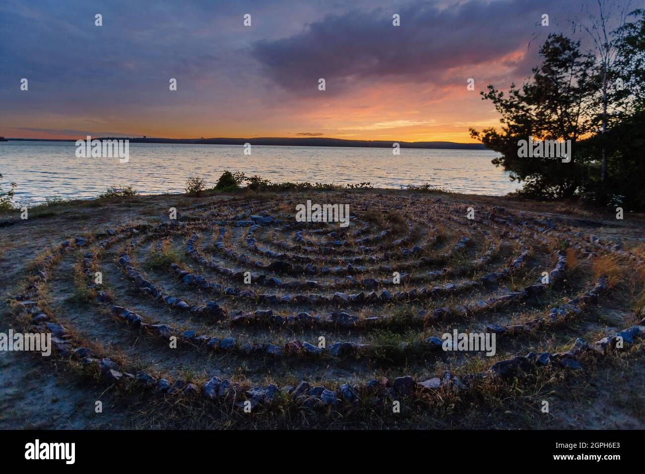 Labirinto a spirale fatto di pietre sulla costa al tramonto Foto Stock