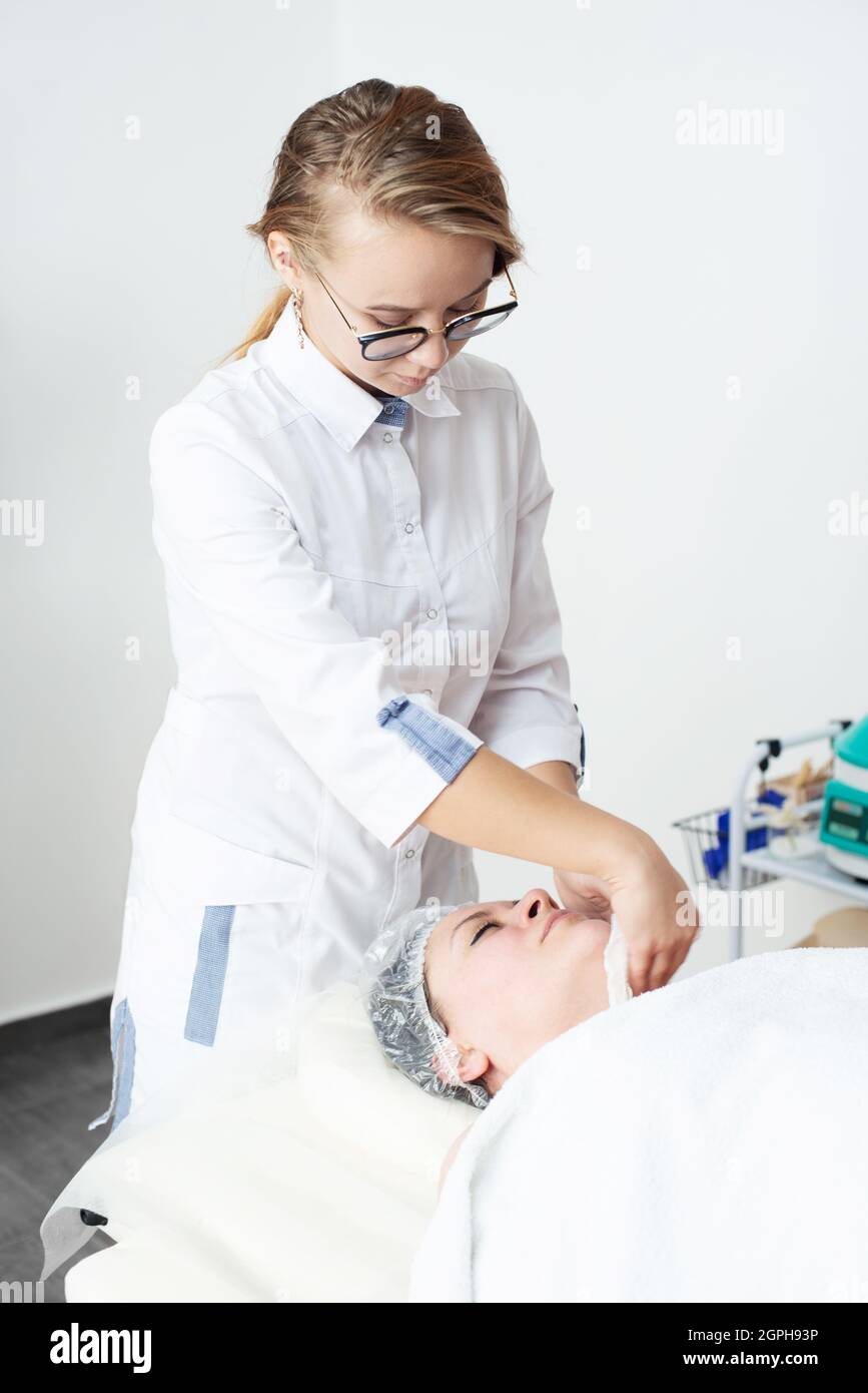 La giovane cosmetologa femminile pulisce il volto di una paziente femminile.trattamento di bellezza facciale.Cosmetologia Foto Stock