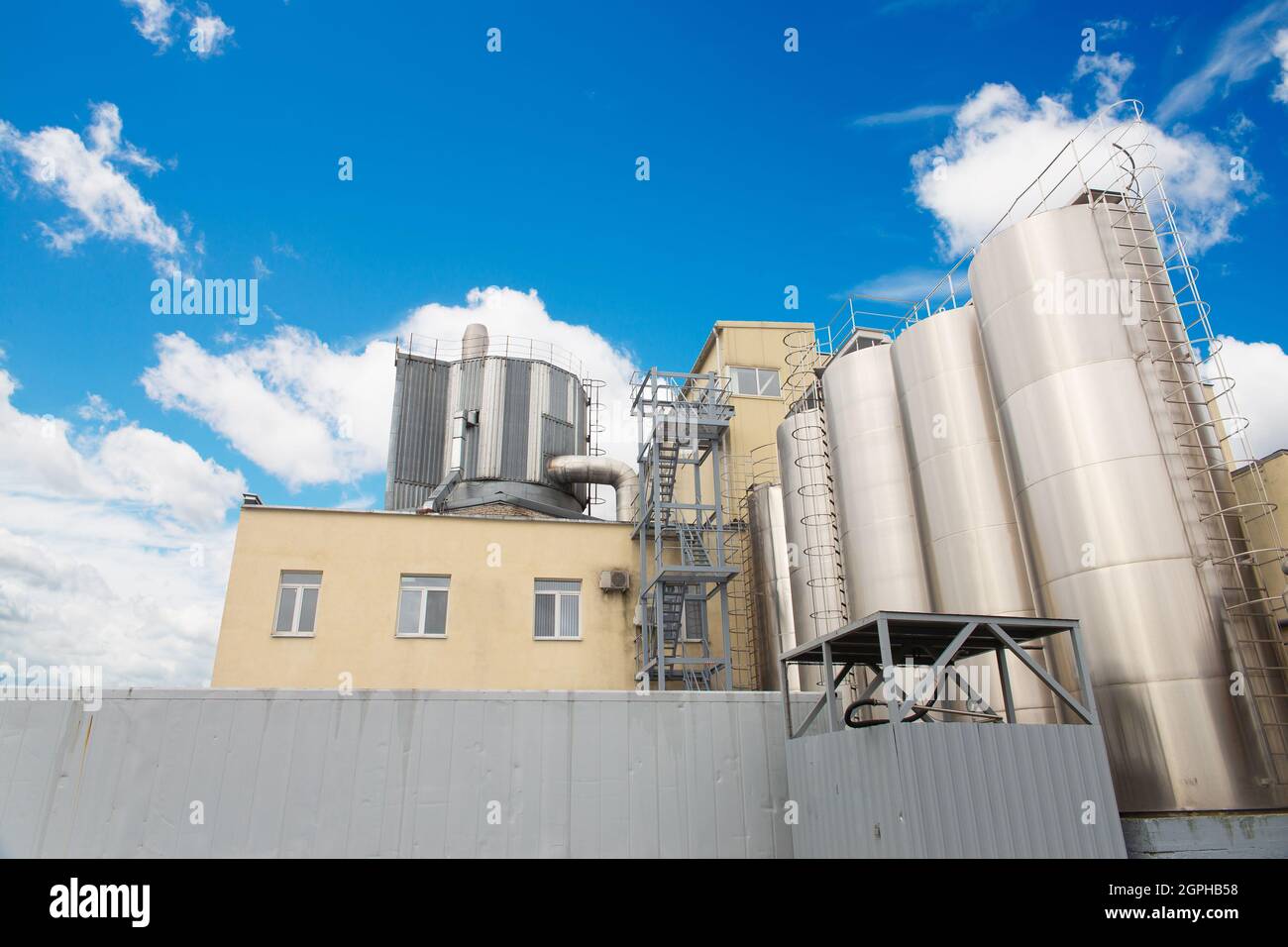 Attrezzatura del serbatoio contro il cielo nuvoloso blu. Industria alimentare o chimica. Produzione su impianto. Foto Stock